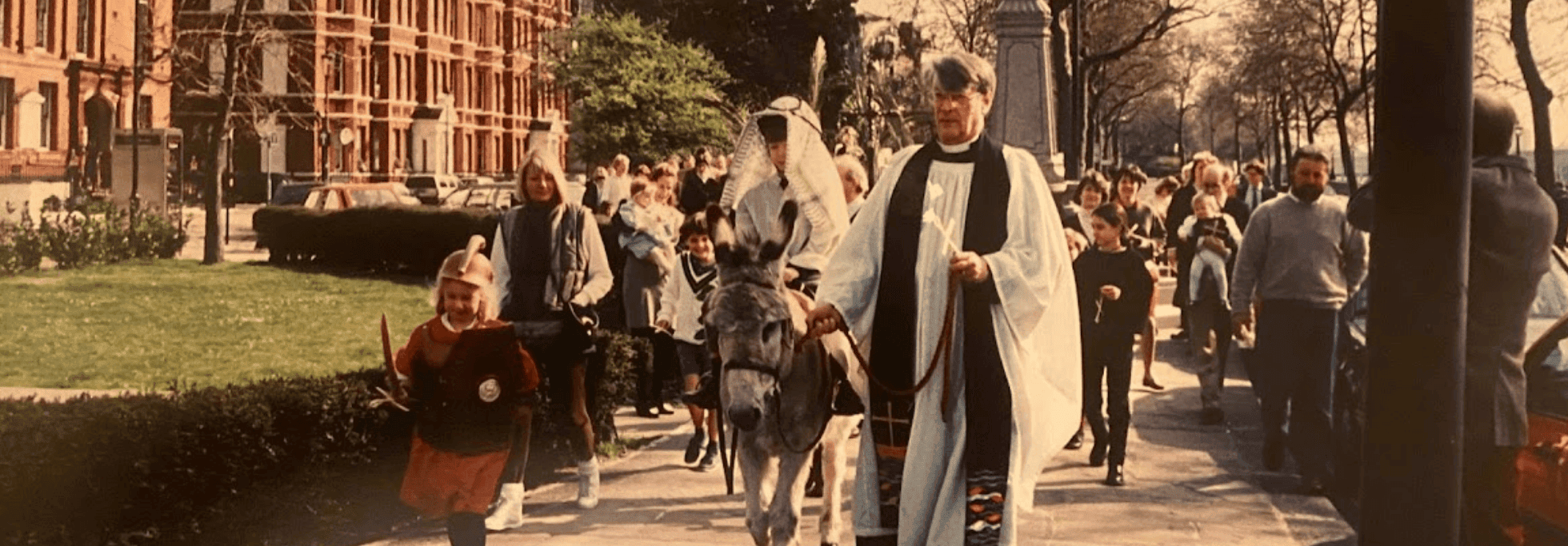 The vicar of Chelsea old church leading a donkey along a path