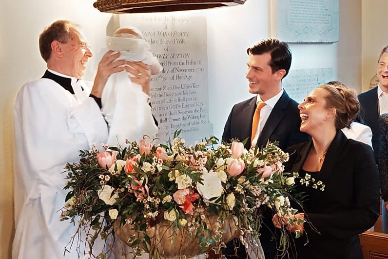 Vicar lifting baby from font during baptism with parents watching
