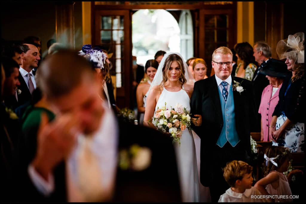 Saffie being walked down the aisle in the church, about to get married. Zac is seen at the front (blurred)